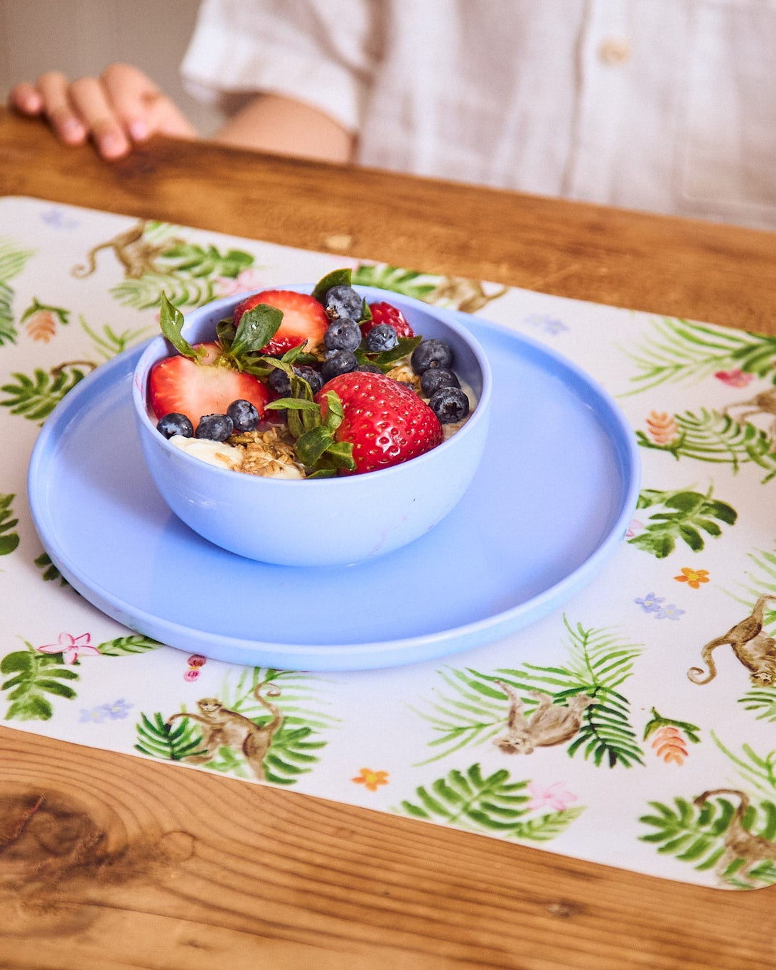 Blue plate and bowl set on a jungle placemat with fresh berries and yogurt