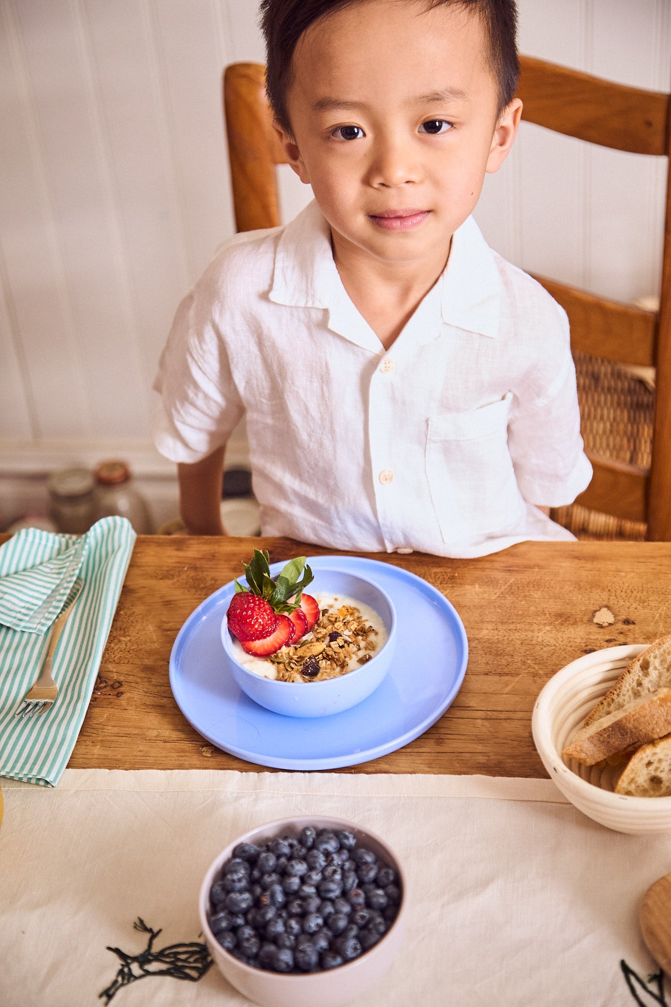 Boy eating fresh berries and yogurt from a pastel blue plate and bowl