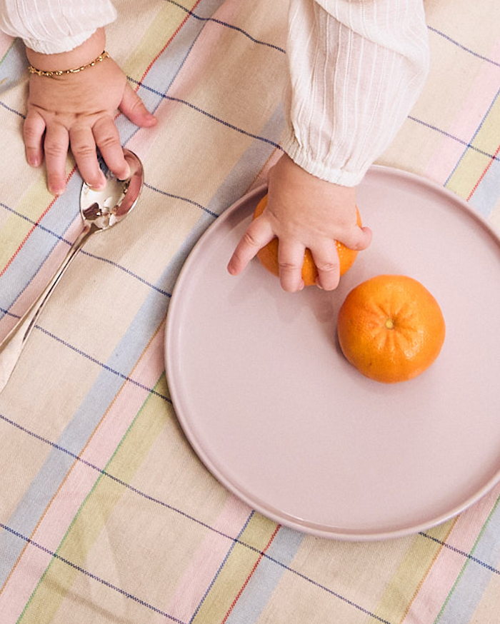 Baby grabbing a fresh clementine from a pastel recette plate