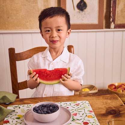 smiling boy eating fruit off pastel dishware