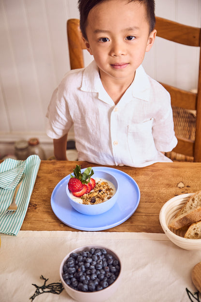 Boy eating fresh berries and yogurt from a pastel blue plate and bowl